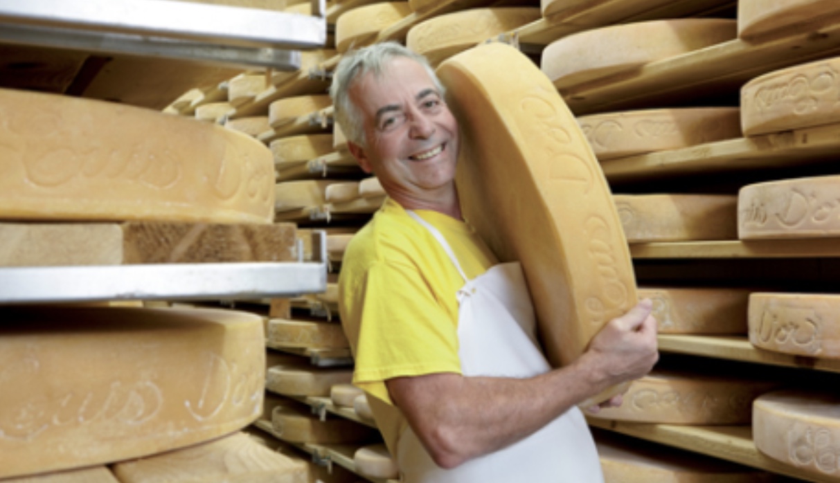 Un homme en tablier présentant un gros morceau de fromage Fromages québécois.