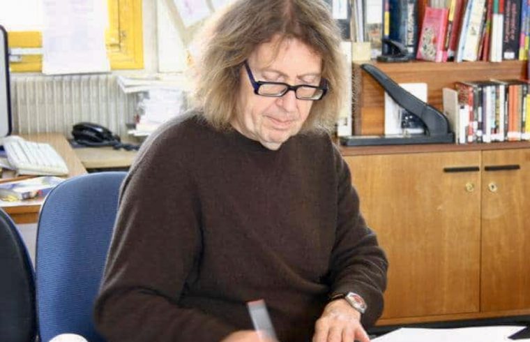 Une femme, portant des lunettes, assise à un bureau entourée de papiers, explore les œuvres poétiques de Claude Beausoleil.