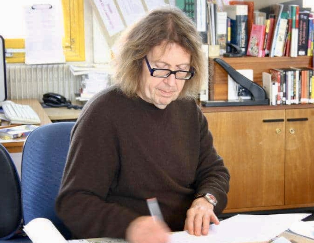 Une femme, portant des lunettes, assise à un bureau entourée de papiers, explore les œuvres poétiques de Claude Beausoleil.