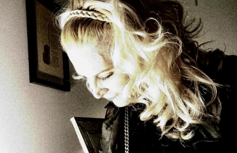 Une femme aux cheveux blonds tient un téléphone portable tout en réfléchissant à la beauté de la poésie.