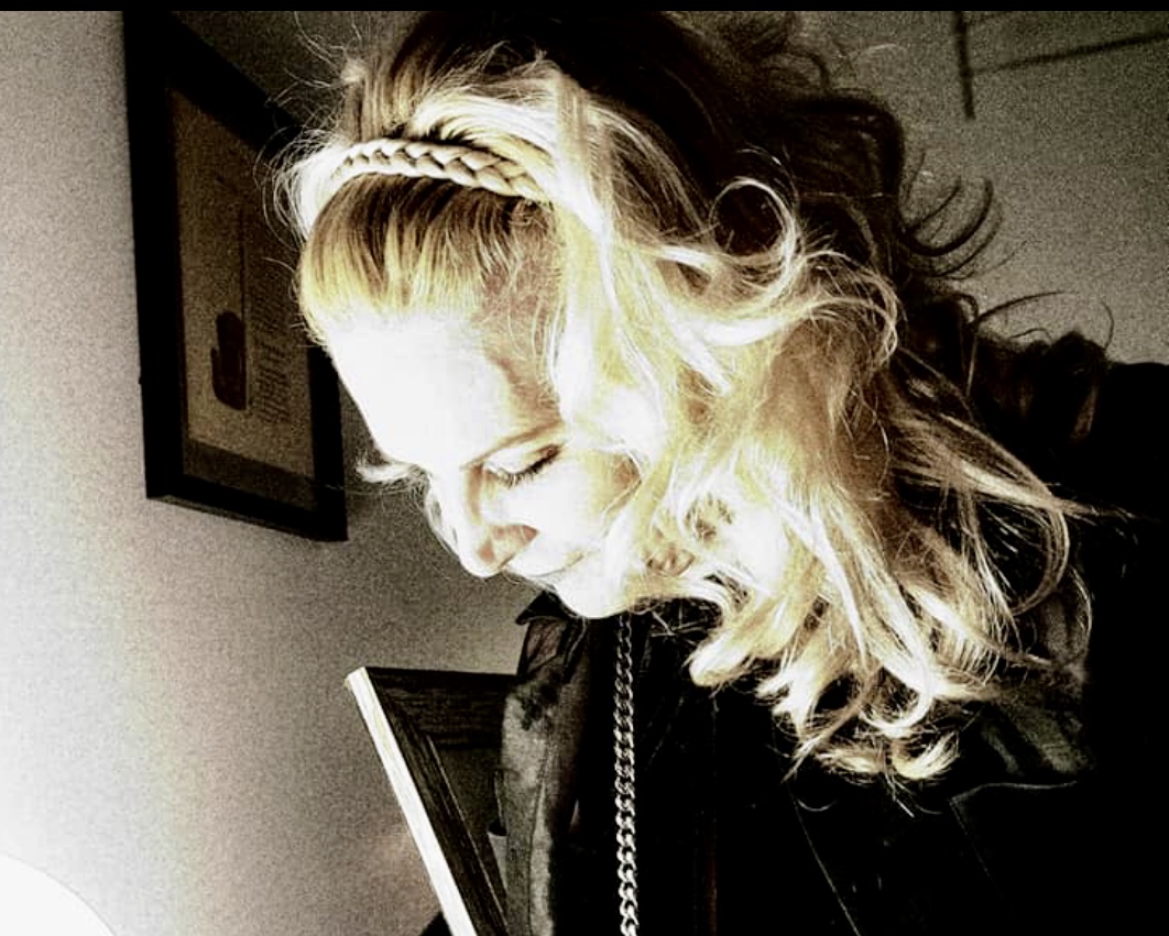 Une femme aux cheveux blonds tient un téléphone portable tout en réfléchissant à la beauté de la poésie.