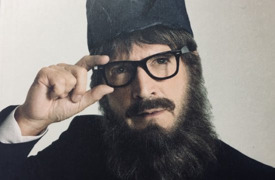 Un homme barbu et à lunettes ajoute de l'humour à une couverture de magazine.
