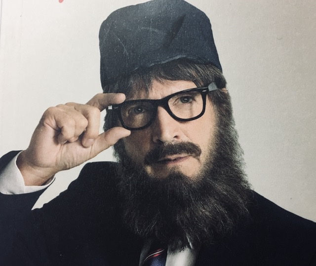 Un homme barbu et à lunettes ajoute de l'humour à une couverture de magazine.