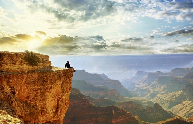 Un homme pratiquant la philosophie spirituelle assis sur une falaise surplombant le grand canyon.