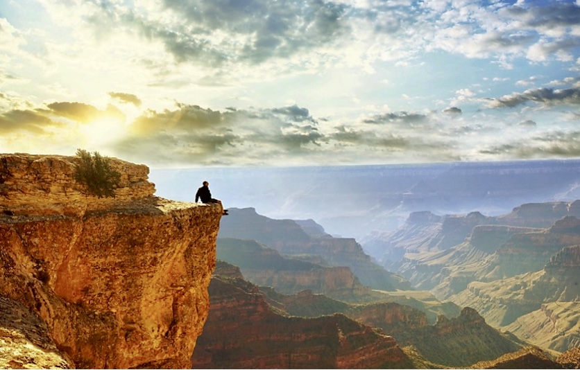 Un homme pratiquant la philosophie spirituelle assis sur une falaise surplombant le grand canyon.