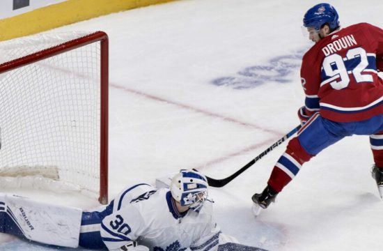 Un joueur de hockey québécois tente de bloquer un tir d'un gardien de but.