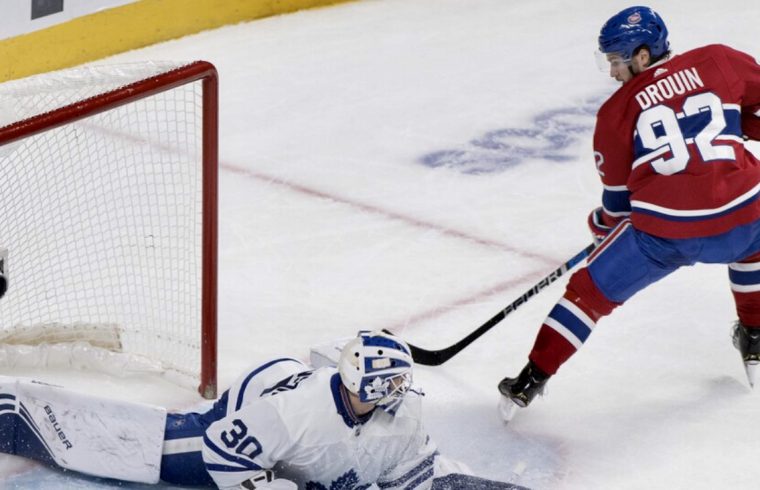 Un joueur de hockey québécois tente de bloquer un tir d'un gardien de but.
