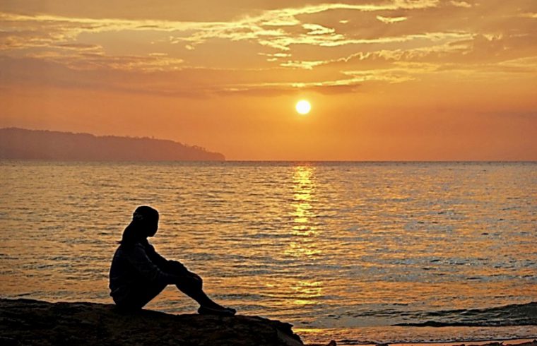 Une personne engagée dans une contemplation spirituelle, assise sur un rocher et observant le coucher de soleil fascinant.