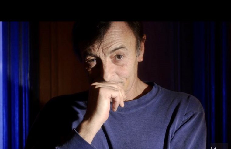 Un homme en chemise bleue réfléchit, la main posée sur son menton, plongé dans la Littérature québécoise.
