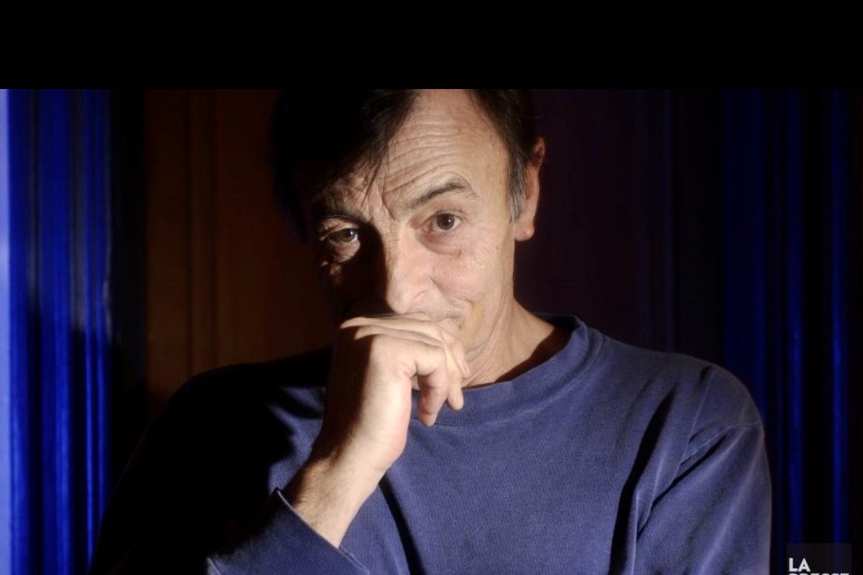 Un homme en chemise bleue réfléchit, la main posée sur son menton, plongé dans la Littérature québécoise.