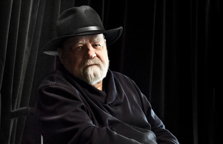 Un homme au chapeau noir, incarnant l'essence de la Littérature québécoise, assis sur une chaise.