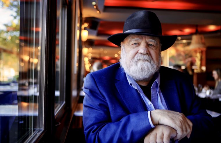 Serge Bouchard, un homme vêtu d'une veste bleue et d'un chapeau, assis dans un restaurant.