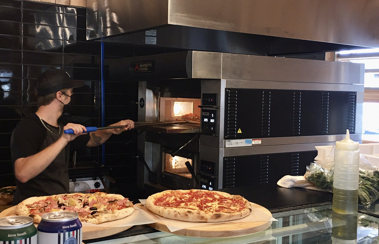 Dans un restaurant italien pittoresque situé à Saint-Sauveur, un homme prépare savamment une pizza dans le four à pizza traditionnel.