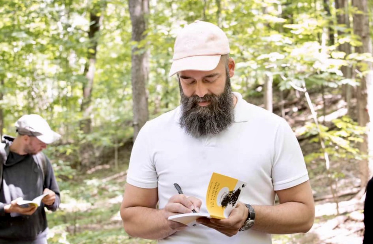 Jonathan Charette, un homme passionné et barbu, écrit dans un carnet dans les bois.