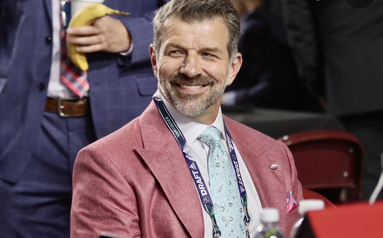 Un homme en costume et cravate roses sourit lors d'un match de hockey.