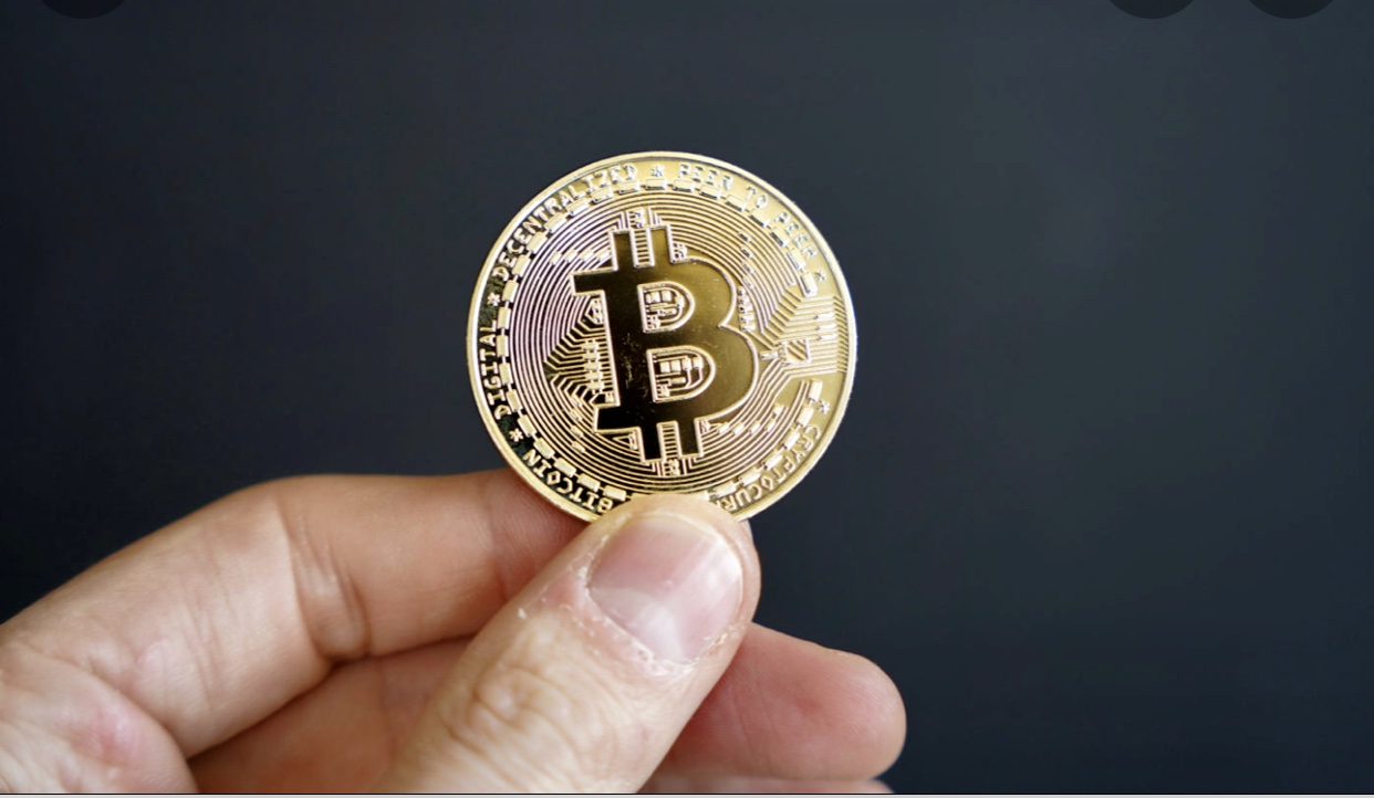 Une personne tenant une pièce de monnaie Bitcoin devant un fond noir pour mettre en valeur l'attrait des Bitcoins.