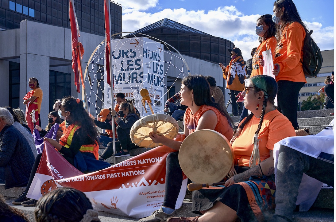 Un groupe de femmes en chemises orange tenant des tambours devant un bâtiment, capturées dans de superbes photographies.