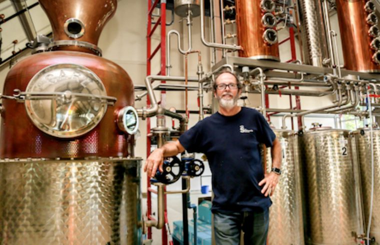 Un homme fièrement debout devant un grand alambic de la distillerie Gin du Québec.