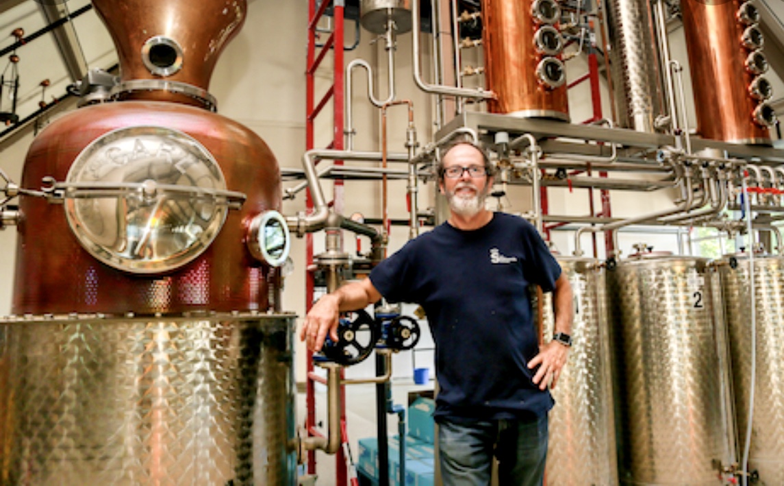 Un homme fièrement debout devant un grand alambic de la distillerie Gin du Québec.