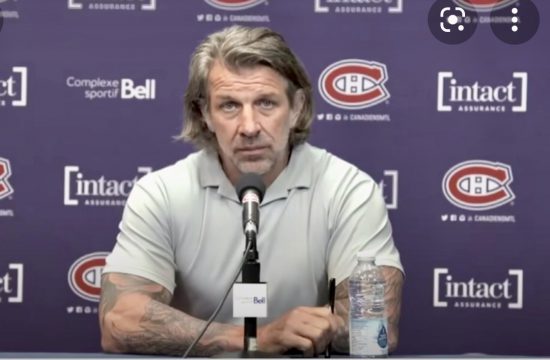 Un homme lors d’une conférence de presse discutant de hockey avec des microphones devant lui.