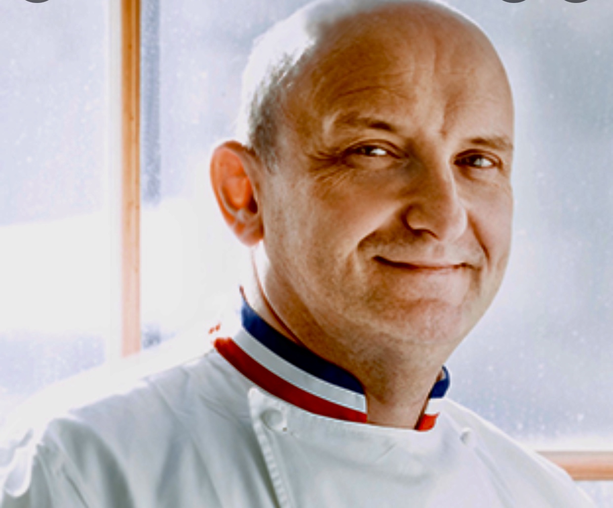 Christian Faure, un homme en uniforme de cuisinier, sourit devant une fenêtre.