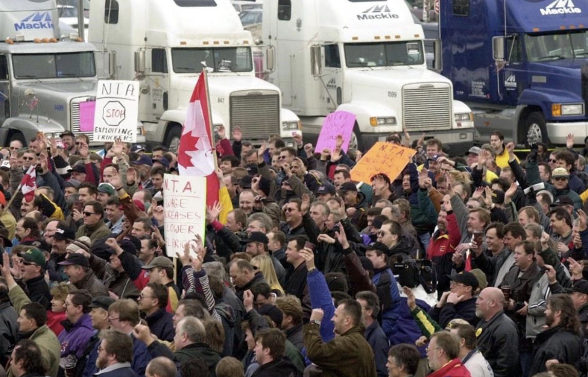 Une foule de personnes brandissant des pancartes prônant Libertés et Covid devant un camion.