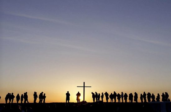 Un groupe de personnes engagées dans une discussion et une réflexion philosophiques debout devant une croix au coucher du soleil.