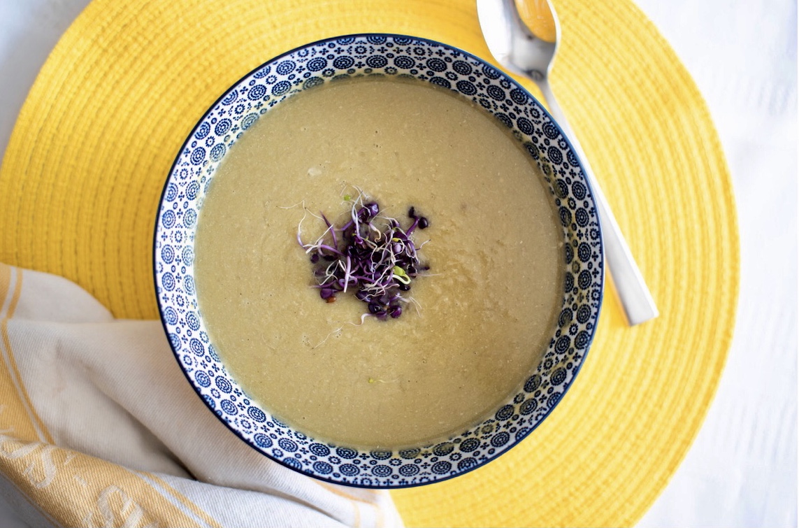 Un bol de soupe de poireaux avec une cuillère sur une assiette jaune.