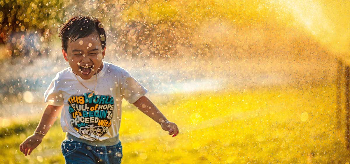 Un jeune garçon profite d'une activité estivale ludique alors qu'il traverse un arroseur dans l'eau rafraîchissante.