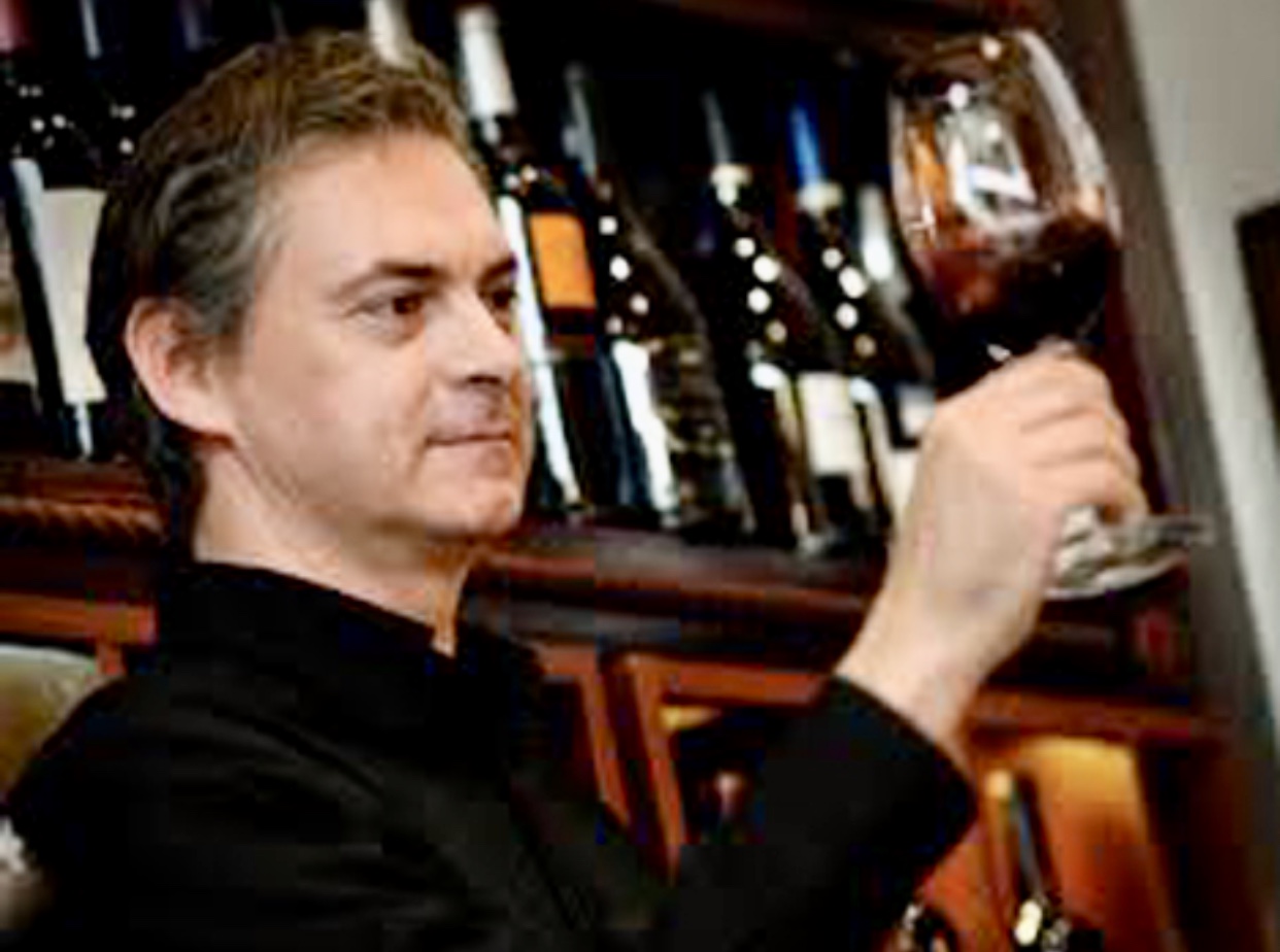 Un homme tenant un verre de vin devant une cave à vins.