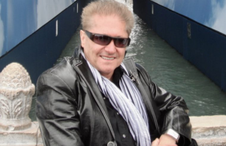 Un homme en veste noire pose devant un canal.