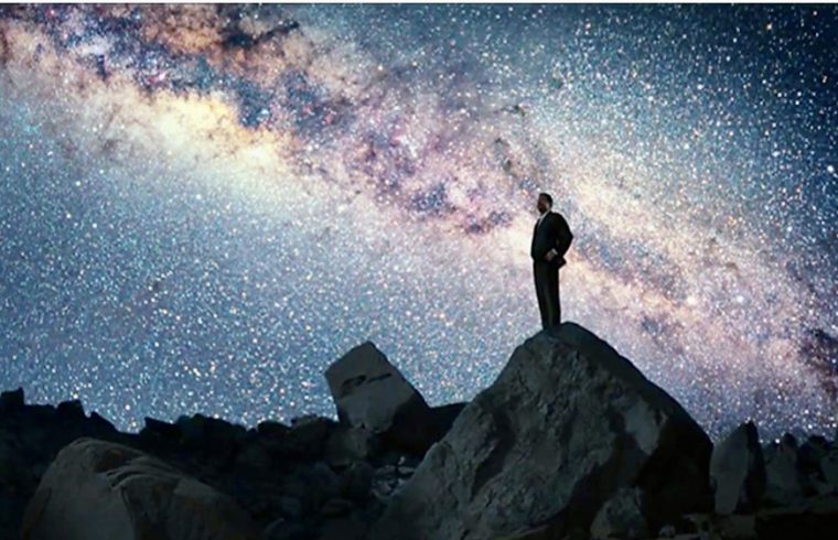 Un homme engagé dans la philosophie debout sur un rocher au milieu d'un ciel étoilé.