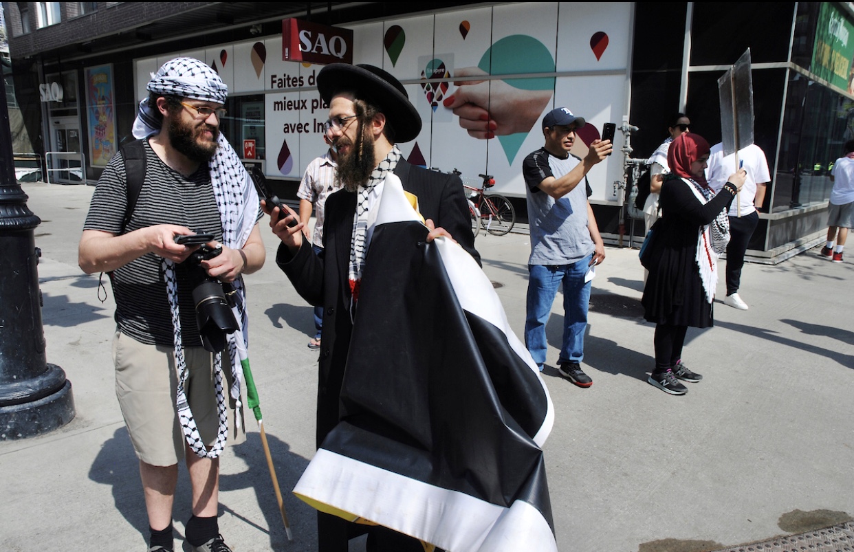 Un groupe de personnes debout sur un trottoir avec un drapeau juif lors d’une manifestation palestinienne.