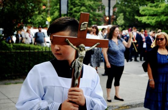Un jeune garçon tenant une croix en bois devant une foule, magnifiquement capturé sur des photographies.