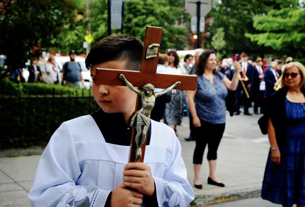 Un jeune garçon tenant une croix en bois devant une foule, magnifiquement capturé sur des photographies.