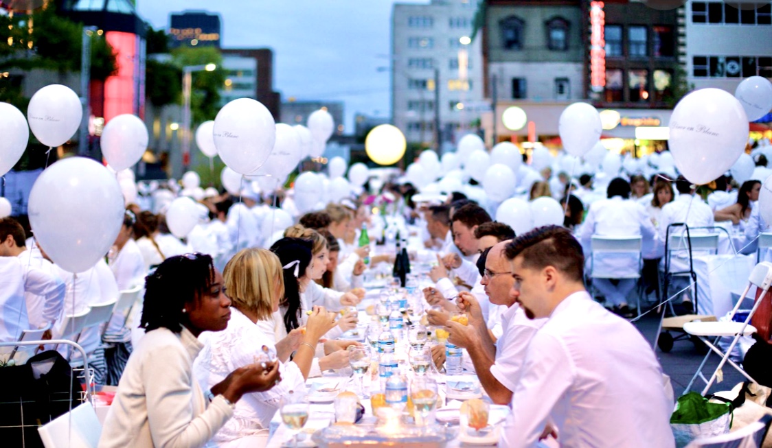 Un groupe de personnes assises à une table ornée de ballons, célébrant le Dîner en blanc 2022.