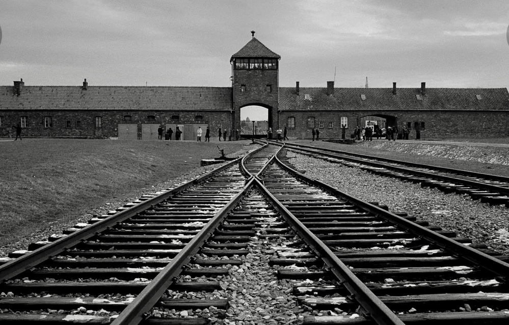 Une photo en noir et blanc d’une voie ferrée devant le camp de concentration d’Auschwitz pendant l’Holocauste.