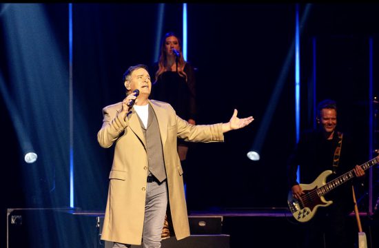 Mario Pelchat, un homme en manteau marron, chante sur scène.