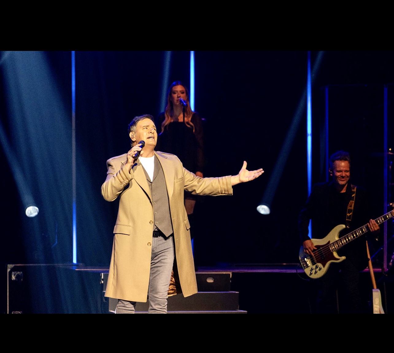 Mario Pelchat, un homme en manteau marron, chante sur scène.