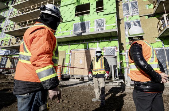 Trois ouvriers en construction devant un bâtiment.