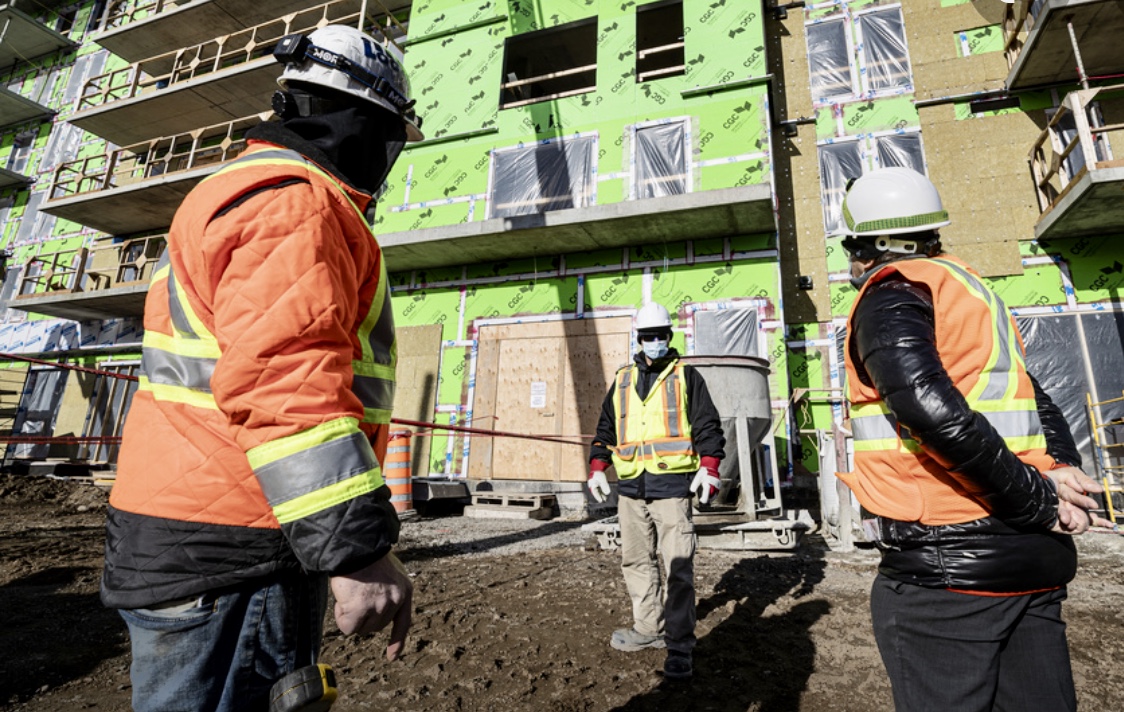 Trois ouvriers en construction devant un bâtiment.