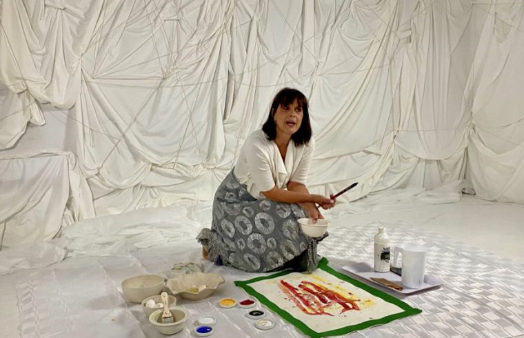 Une femme assise par terre avec un pinceau. (Arts visuels)