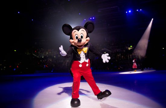 Une mascotte Disney habillée en Mickey Mouse glissant gracieusement sur une patinoire.