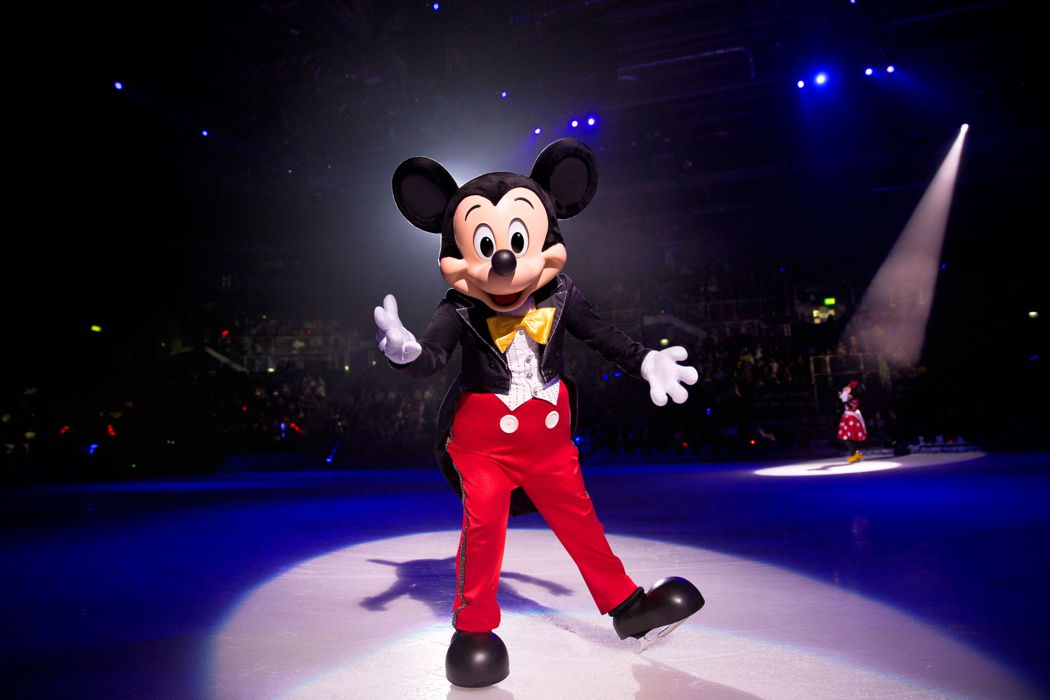 Une mascotte Disney habillée en Mickey Mouse glissant gracieusement sur une patinoire.