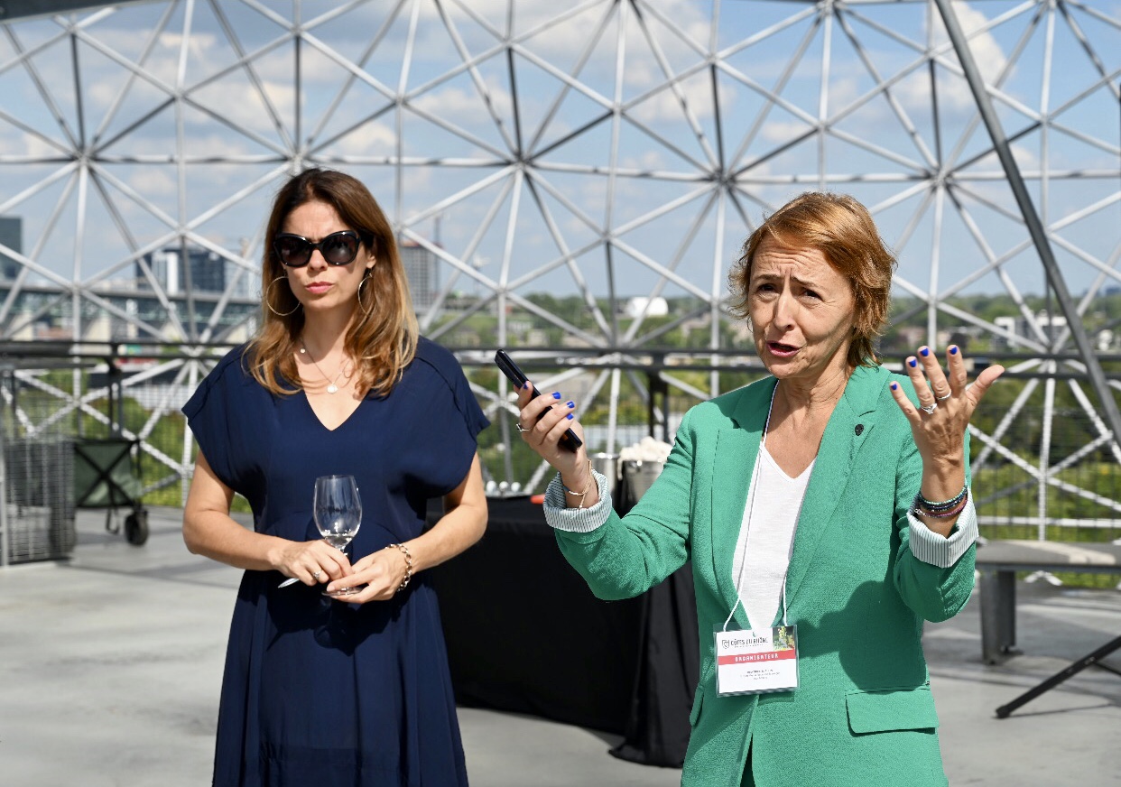 Deux femmes debout devant une coupole de verre ornée de vins exquis.