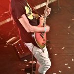 Un homme du groupe Bran Van 3000 jouant de la guitare sur scène avec des confettis.