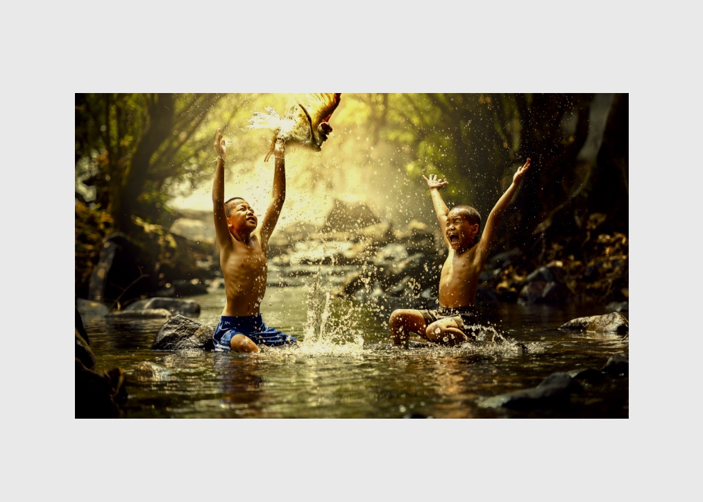 Deux garçons barbotent dans une rivière avec un oiseau planant au-dessus de leur tête.