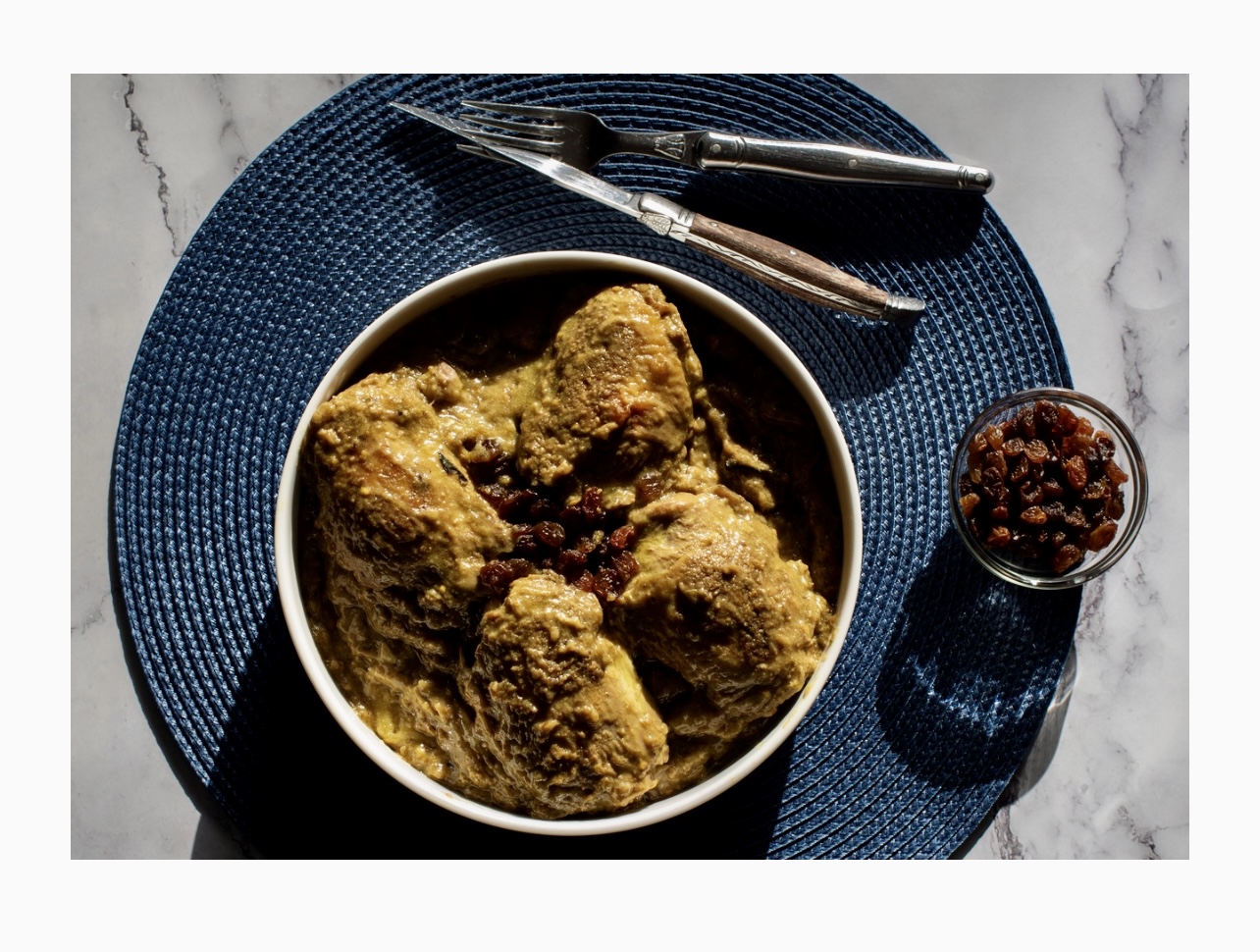 Recettes : Un bol de poulet et de raisins secs sur une assiette bleue.