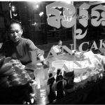 Une femme se tient devant une boulangerie la nuit au Cambodge, en capturant l'essence avec "Photos du Cambodge".