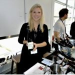 Une femme tenant une bouteille de vin Vins d’Autriche devant une table.
